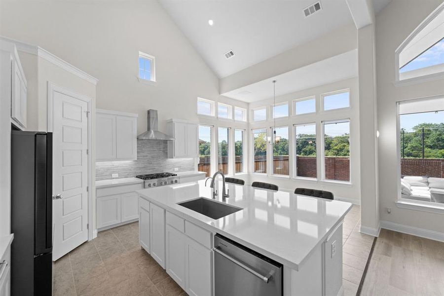 Kitchen featuring black refrigerator, an island with sink, dishwasher, plenty of natural light, and wall chimney range hood