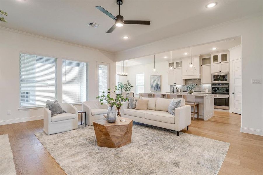 Living room with crown molding, sink, ceiling fan with notable chandelier, and light wood-type flooring