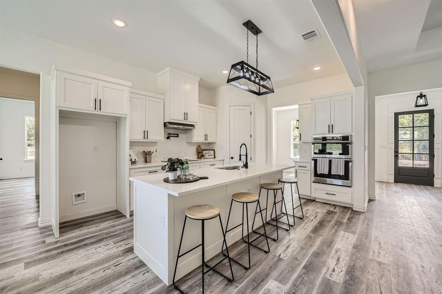 Kitchen with white cabinets, a center island with sink, a healthy amount of sunlight, and stainless steel double oven