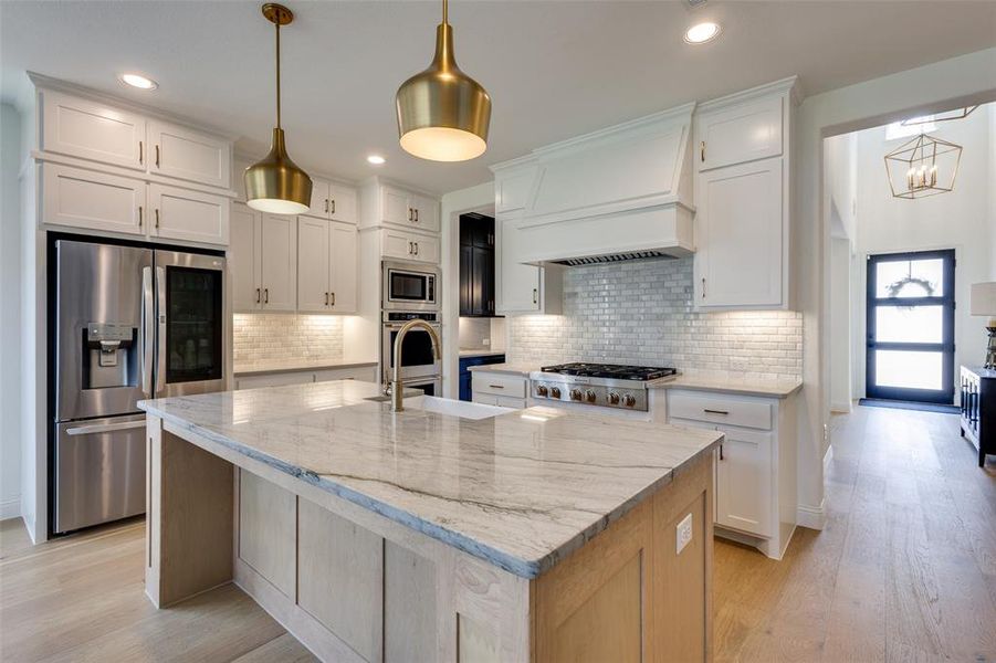 Kitchen with backsplash, premium range hood, stainless steel appliances, and an island with sink