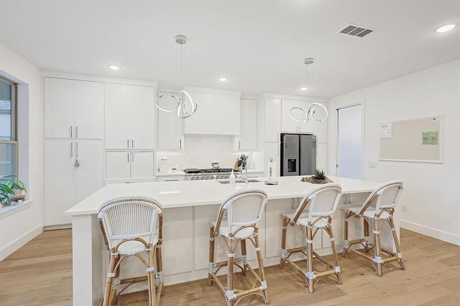 Kitchen featuring stainless steel refrigerator with ice dispenser, a kitchen island with sink, hanging light fixtures, and light wood-type flooring