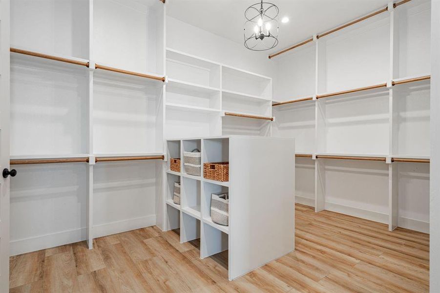 Example of builders Walk in closet with light wood-type flooring and an inviting chandelier