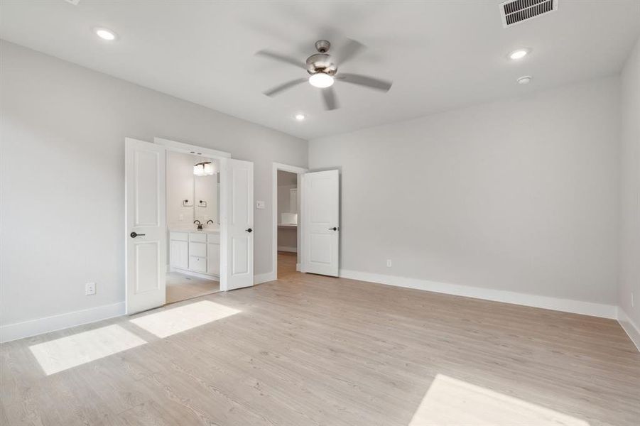 Unfurnished bedroom with ensuite bathroom, ceiling fan, and light hardwood / wood-style floors