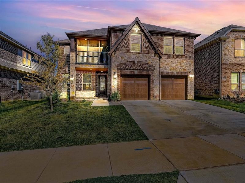 View of front of home with central AC, a yard, a garage, and a balcony