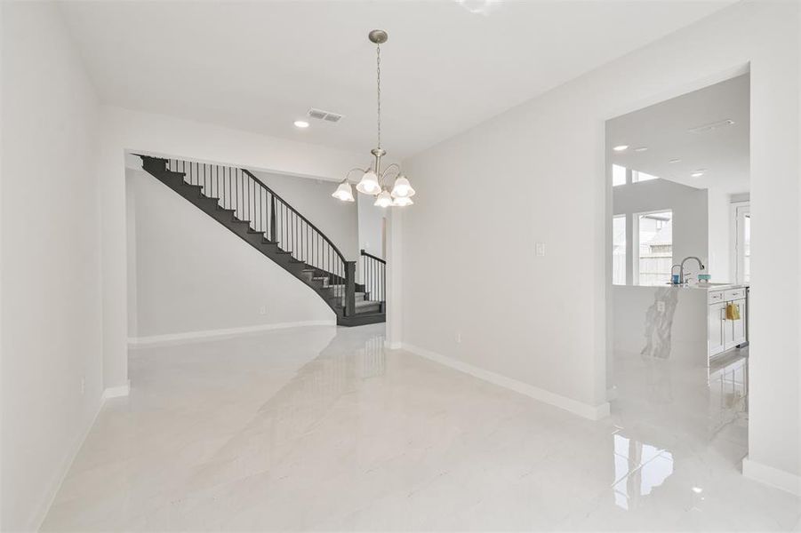 The photo shows a bright, spacious entryway with polished white tile flooring and a modern staircase with dark railings. The neutral color palette offers a blank canvas for personalization. A peek into the adjacent room suggests a sleek kitchen area.