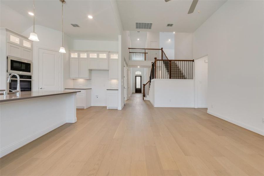 Unfurnished living room with light hardwood / wood-style flooring, ceiling fan, and a towering ceiling