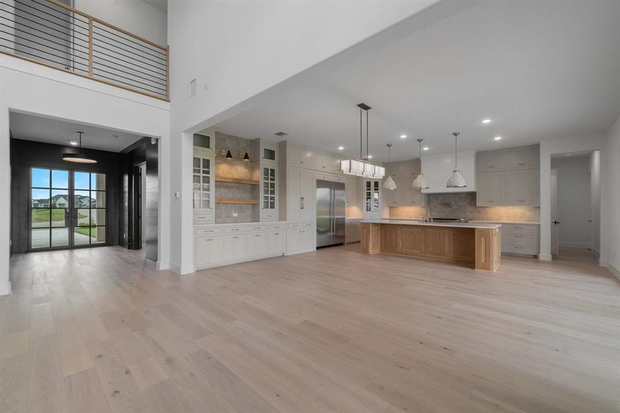 Kitchen with stainless steel built in fridge, pendant lighting, light wood-type flooring, a center island with sink, and backsplash