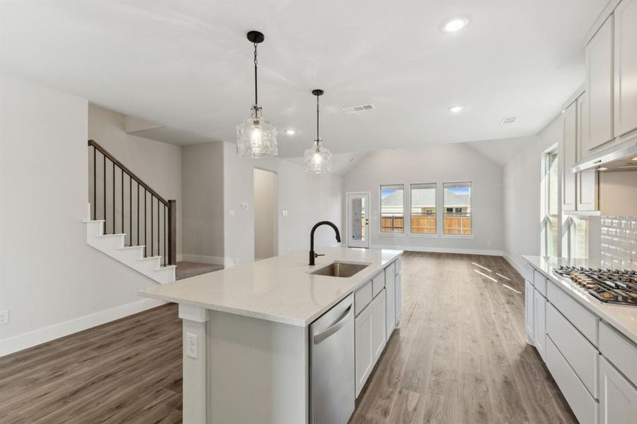 Kitchen featuring stainless steel appliances, lofted ceiling, white cabinets, hardwood / wood-style floors, and a kitchen island with sink