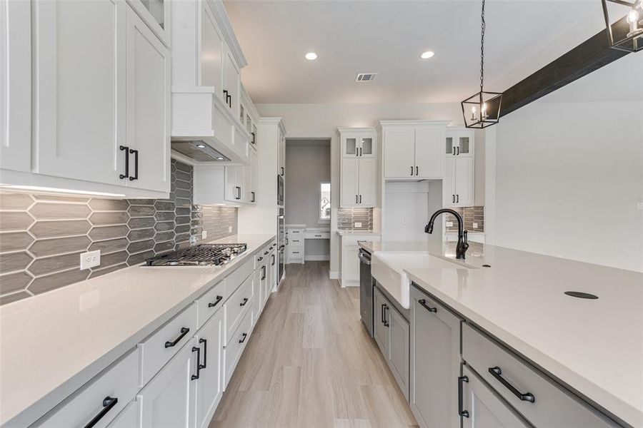 Kitchen with sink, white cabinets, hanging light fixtures, decorative backsplash, and stainless steel appliances