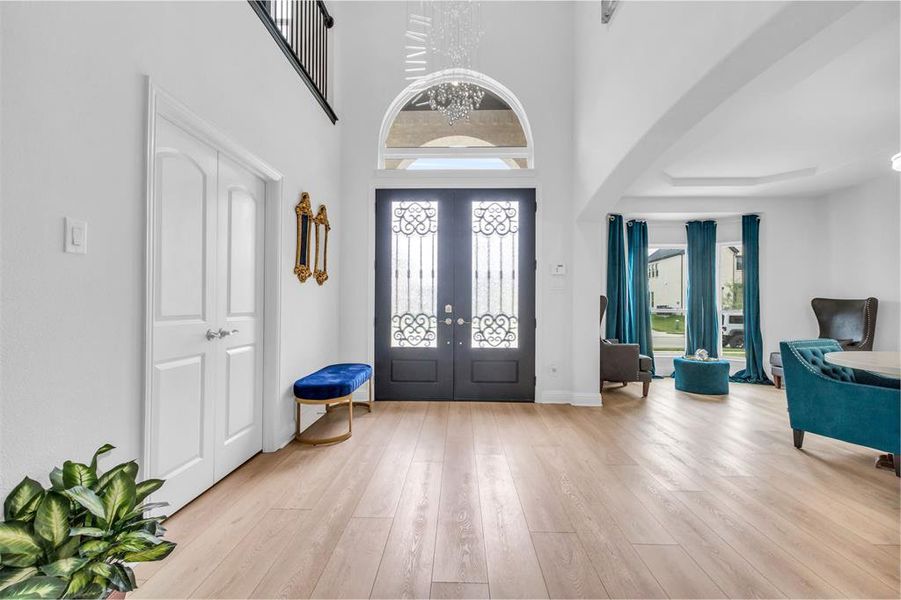 Entryway featuring a high ceiling, french doors, light hardwood / wood-style flooring, and a notable chandelier