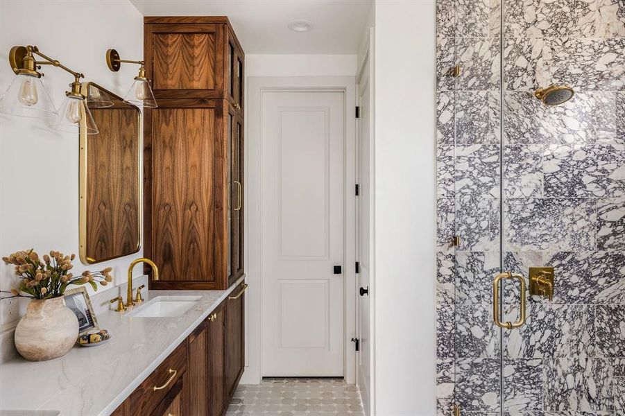 Primary bath features walnut cabinetry and  custom marble tile shower.