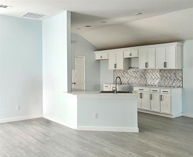 Kitchen with tasteful backsplash, sink, white cabinetry, vaulted ceiling, and light hardwood / wood-style flooring