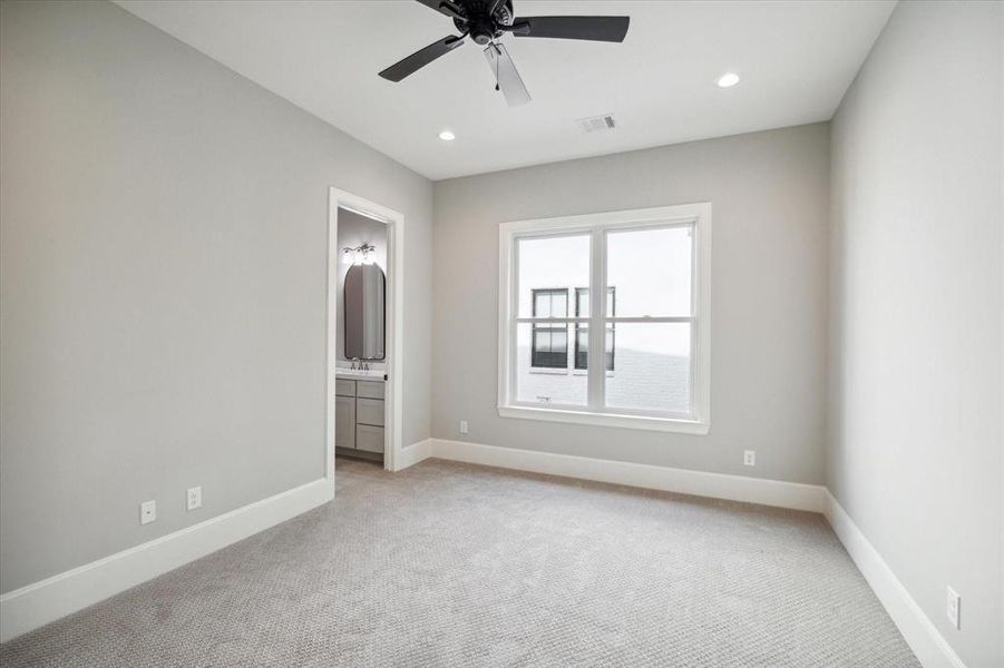 This is a bright, unfurnished room with neutral walls and carpeted flooring, featuring a ceiling fan and a window that allows for natural light. The room also has a built-in closet for storage.