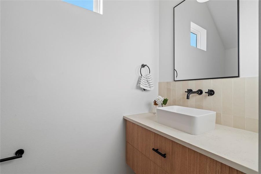 This hall bath combines understated elegance with modern design. Featuring a sleek vessel sink and matte black fixtures, the space is accentuated by soft neutral tones and clean lines, creating a calming and functional atmosphere ideal for everyday use.