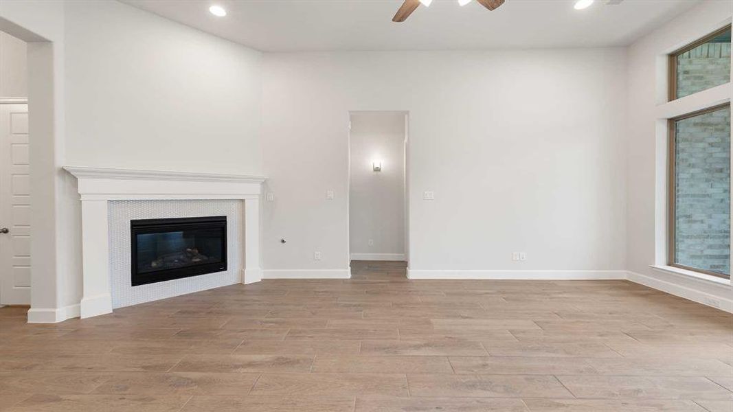 Unfurnished living room featuring a tile fireplace, ceiling fan, and light hardwood / wood-style floors