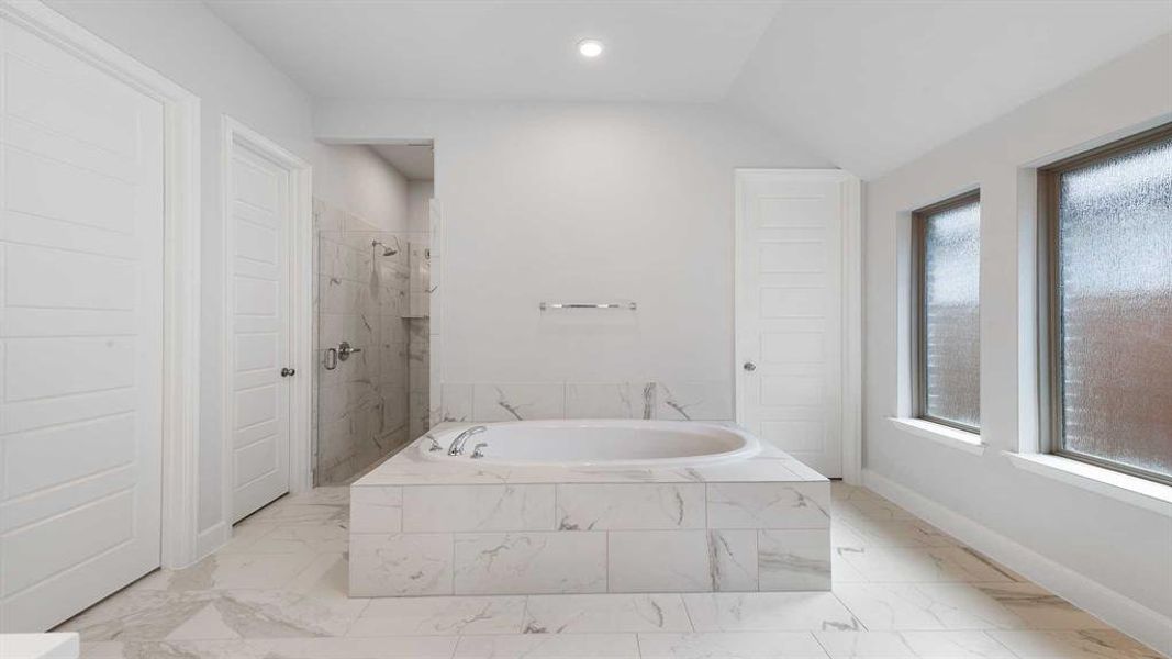 Bathroom featuring a healthy amount of sunlight, vaulted ceiling, and shower with separate bathtub