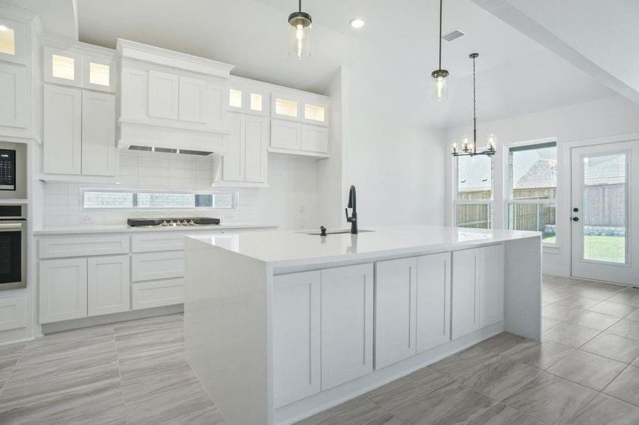 Kitchen featuring white cabinets, hanging light fixtures, backsplash, and an island with sink