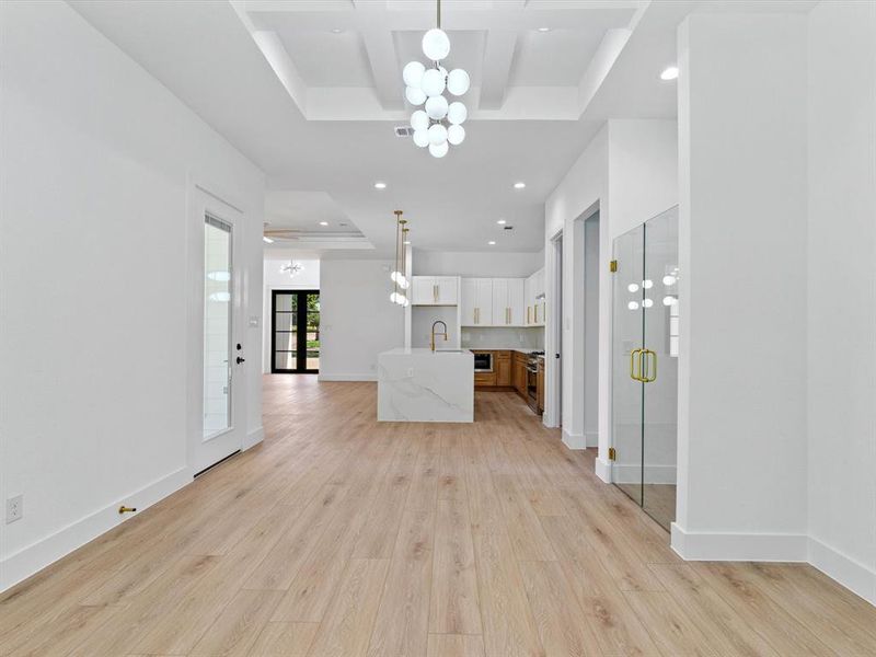 Unfurnished living room with coffered ceiling, sink, a raised ceiling, and light hardwood / wood-style floors