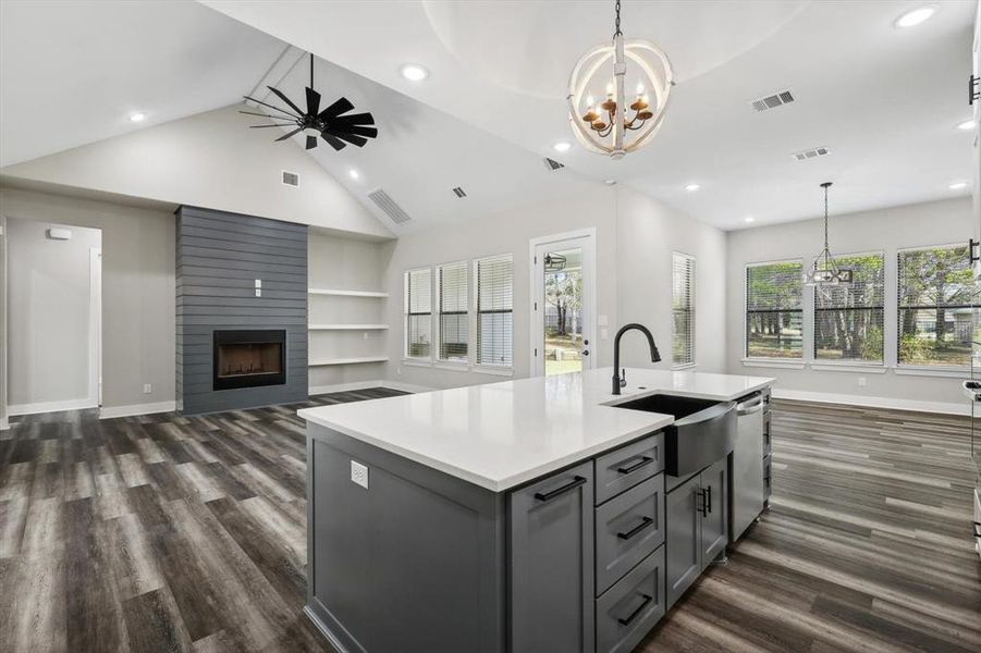 Kitchen with an island with sink, dark wood-type flooring, sink, and a large fireplace