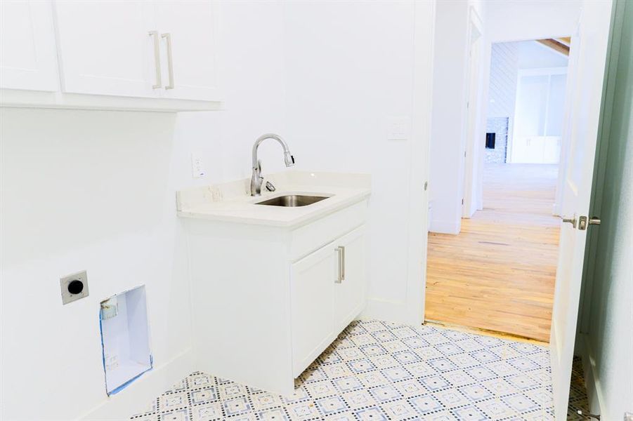 Clothes washing area with light hardwood / wood-style floors, sink, cabinets, and hookup for an electric dryer