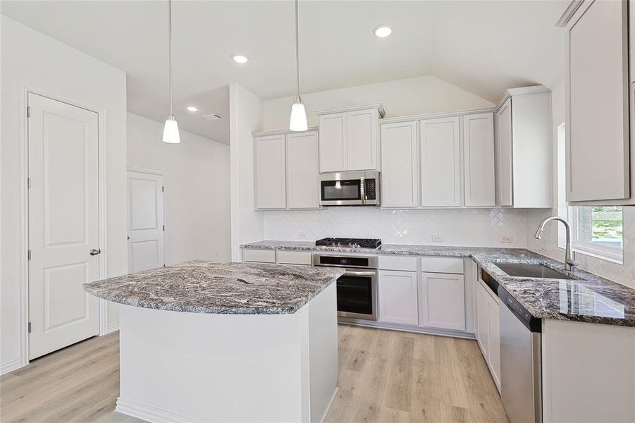 Kitchen with light hardwood / wood-style flooring, stainless steel appliances, a center island, sink, and white cabinets