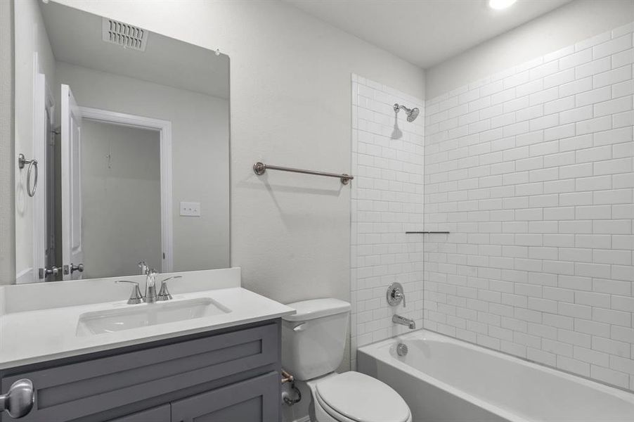 Full bathroom featuring vanity, tiled shower / bath combo, and toilet