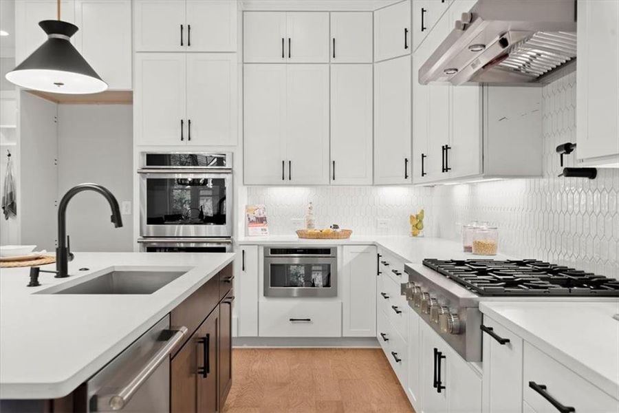 Kitchen with light hardwood / wood-style floors, decorative light fixtures, sink, white cabinets, and wall chimney exhaust hood