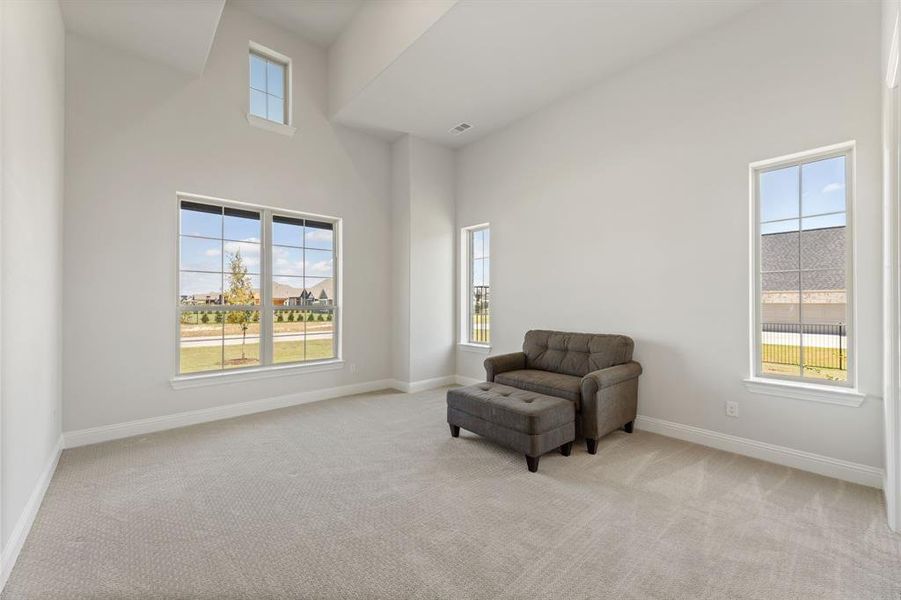 Sitting room with a towering ceiling, light colored carpet, and plenty of natural light