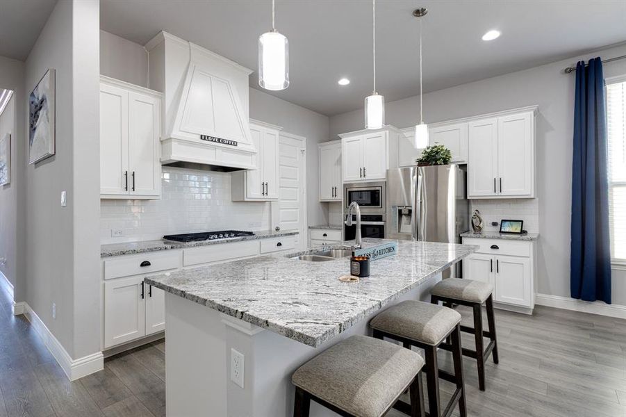 Kitchen featuring light hardwood / wood-style floors, an island with sink, white cabinetry, custom exhaust hood, and stainless steel appliances