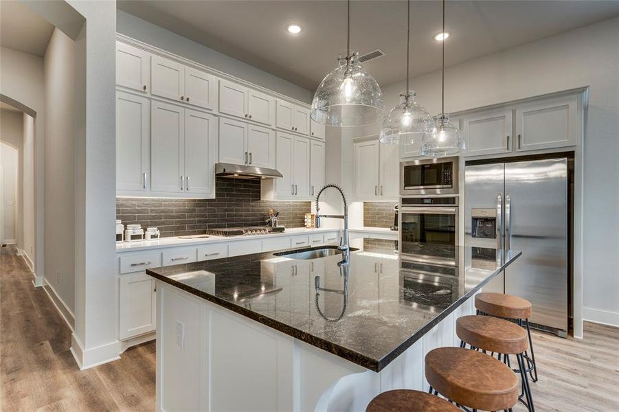 Kitchen featuring stainless steel appliances, sink, backsplash, light hardwood / wood-style floors, and an island with sink