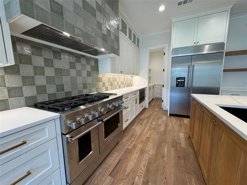 Kitchen featuring premium appliances, custom exhaust hood, white cabinets, light hardwood / wood-style flooring, and backsplash