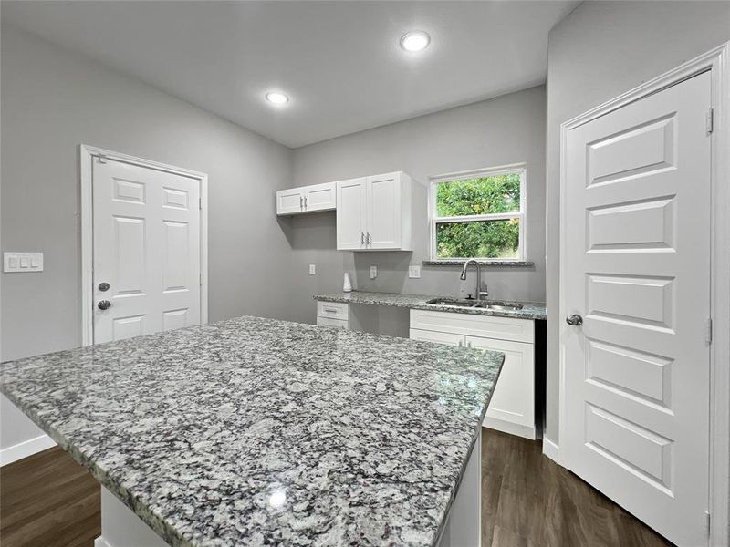 Kitchen featuring a kitchen island, light stone countertops, white cabinetry, and sink