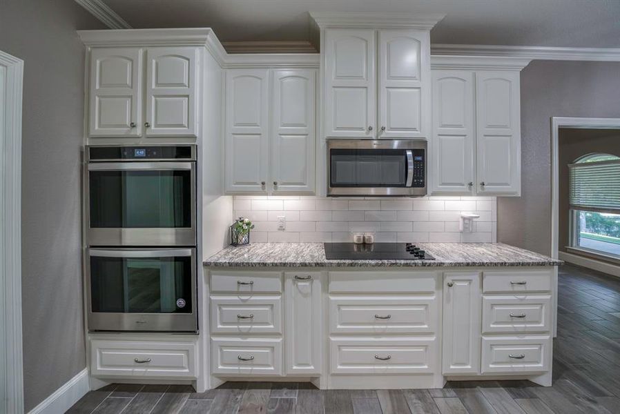 Kitchen with decorative backsplash, stainless steel appliances, double ovens, tile flooring, and white cabinetry