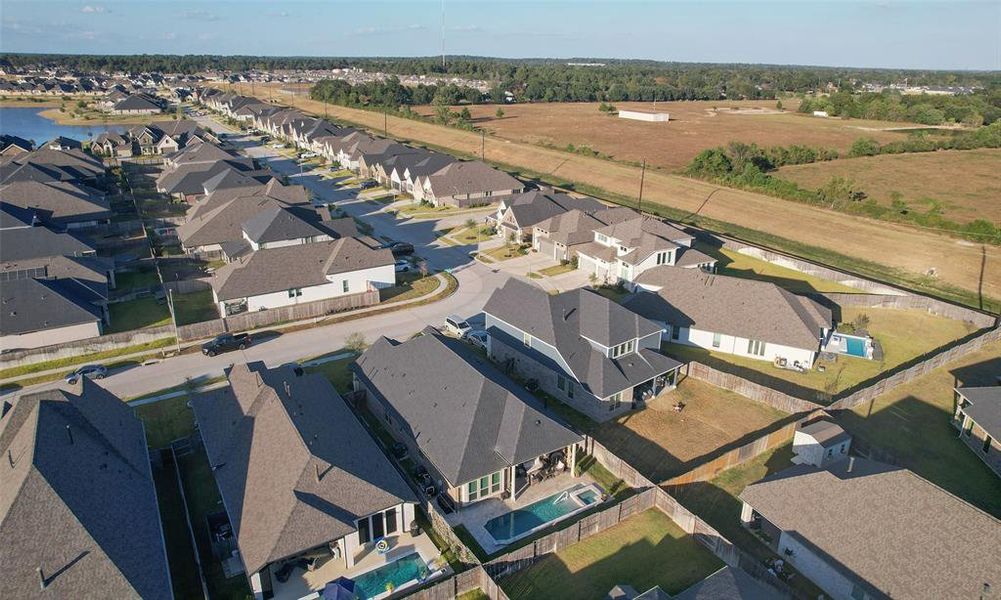 This is an aerial view of a suburban neighborhood with modern single-family homes, some with pools, and well-manicured lawns, adjacent to open land, indicating potential for community growth or natural surroundings.