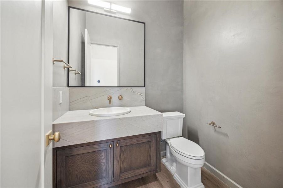 This sleek powder room showcases a modern vanity with dark wood cabinetry, a Azzura Bay marble countertop with leather finish, and minimalist fixtures. The wall-mounted faucet and round sink add a contemporary touch to this elegant space.