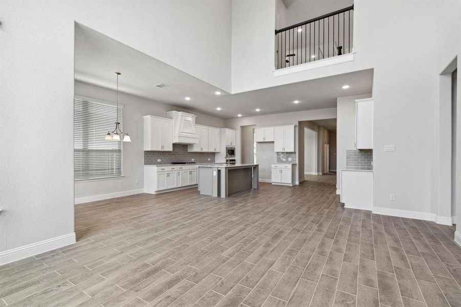 Kitchen with an island with sink, white cabinets, a high ceiling, light hardwood / wood-style flooring, and custom exhaust hood