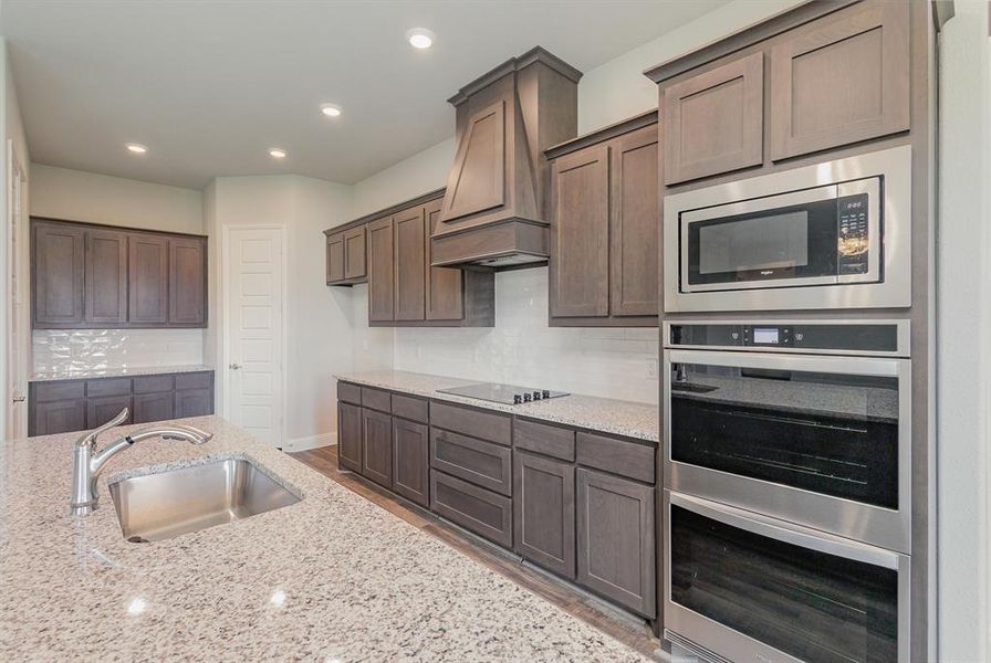 Kitchen with light stone counters, dark brown cabinetry, sink, tasteful backsplash, and appliances with stainless steel finishes