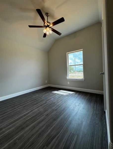 Spare room with ceiling fan, lofted ceiling, and dark wood-type flooring