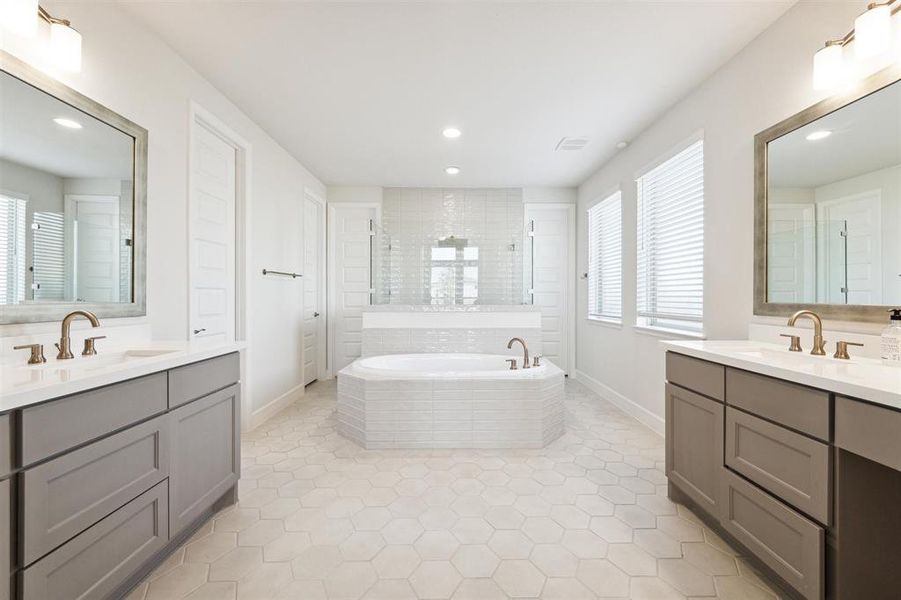 The en-suite primary bath, as viewed when entering, offers split vanities with quartz tops and undermount sinks. The vanity at the right of this photo has a dressing area.