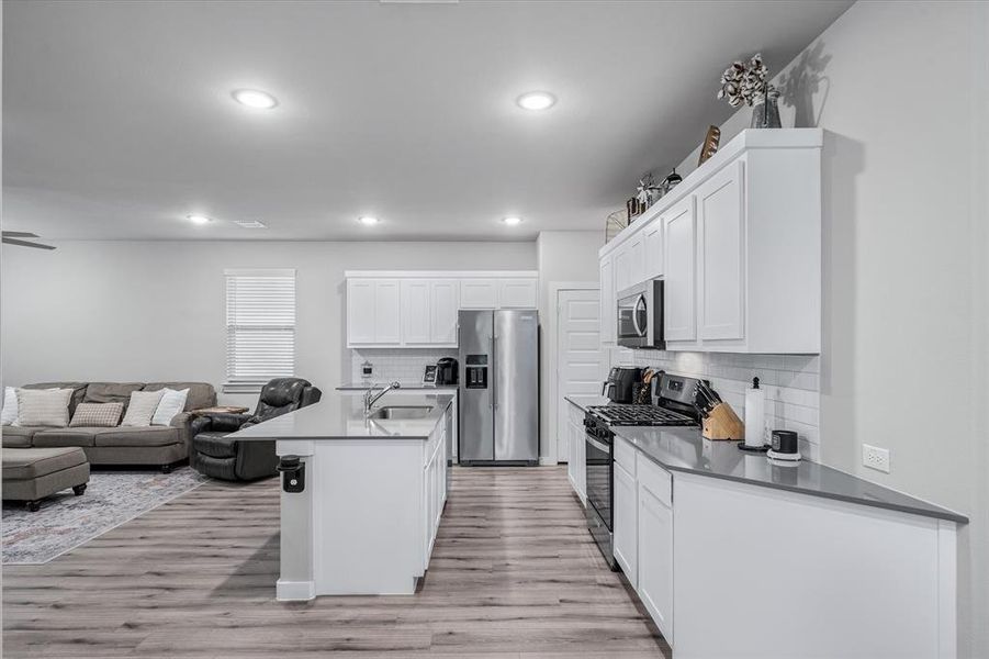 Kitchen featuring light wood-type flooring, stainless steel appliances, an island with sink, sink, and tasteful backsplash