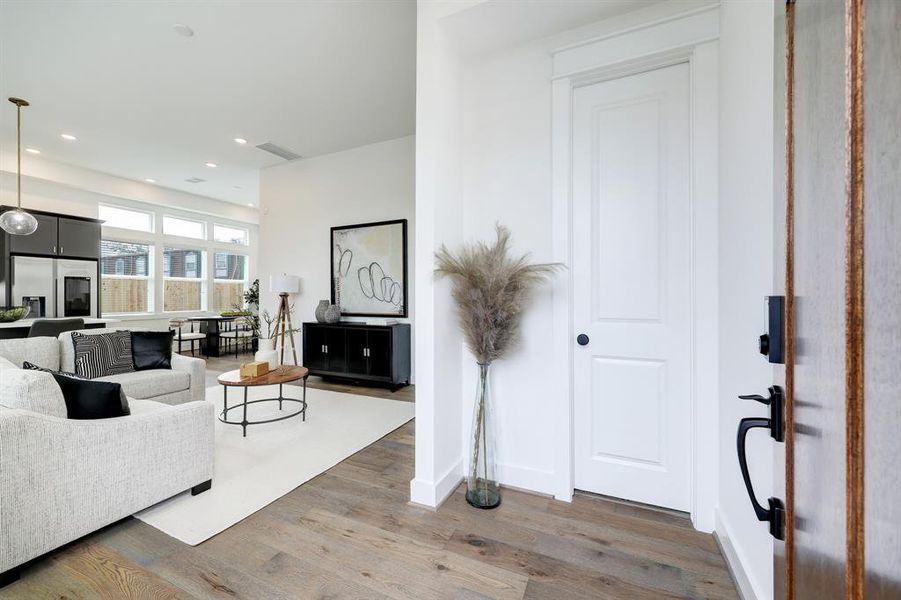 Welcome to an inviting foyer that opens into a spacious, light-filled living area, adorned with chic decor and warm wood flooring.