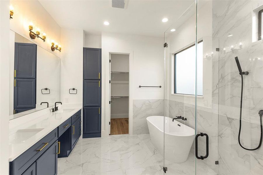 this first floor primary bath has his and hers closets, custom cabinetry, glass enclosed oversized shower as well as a freestanding soaking tub