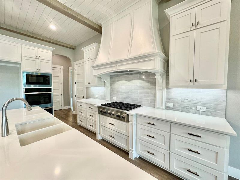 Kitchen featuring white cabinets, appliances with stainless steel finishes, custom exhaust hood, beamed ceiling, and sink