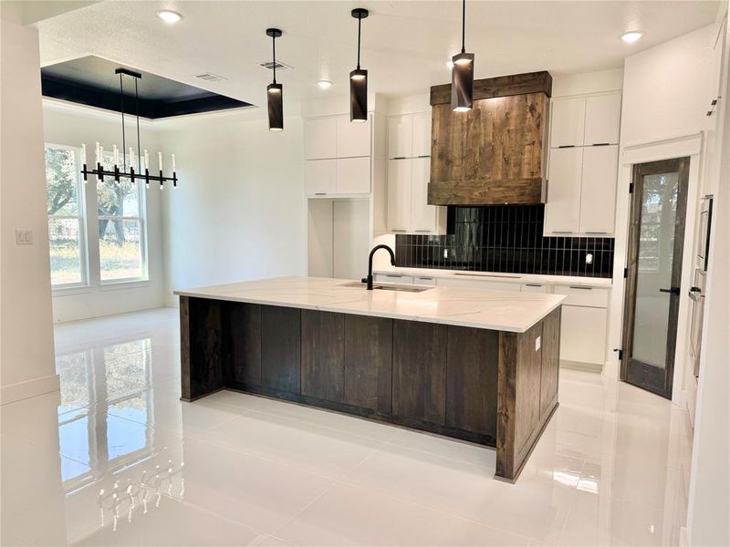 Kitchen with a large island, tasteful backsplash, white cabinetry, and pendant lighting