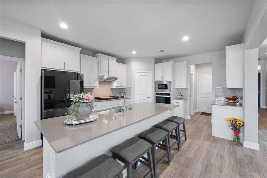 Kitchen featuring stainless steel appliances, a kitchen bar, tasteful backsplash, and white cabinetry