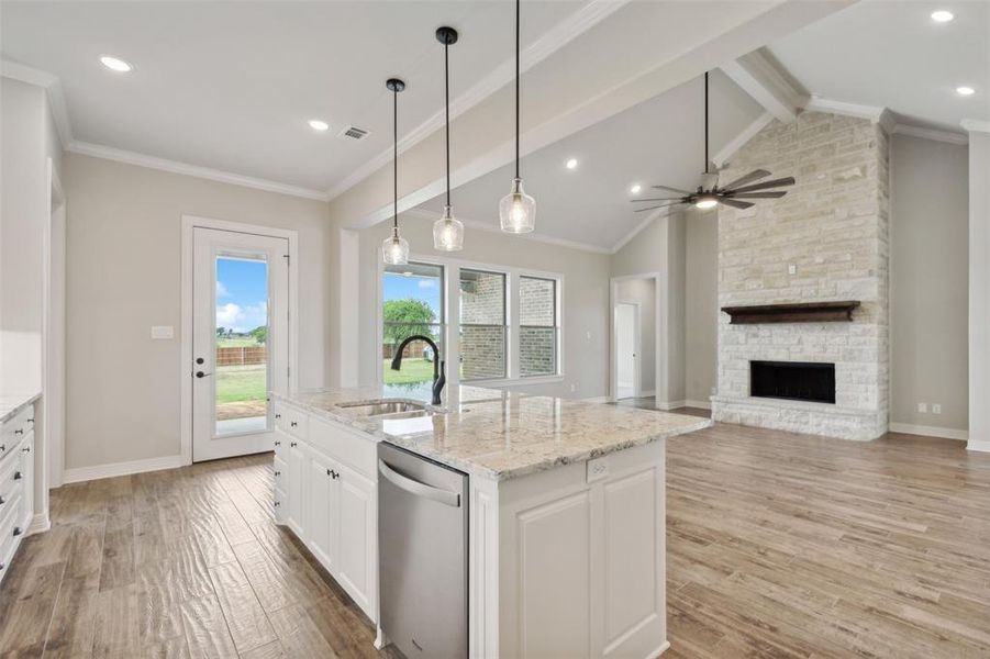 Kitchen featuring ceiling fan, vaulted ceiling with beams, sink, dishwasher, and a fireplace