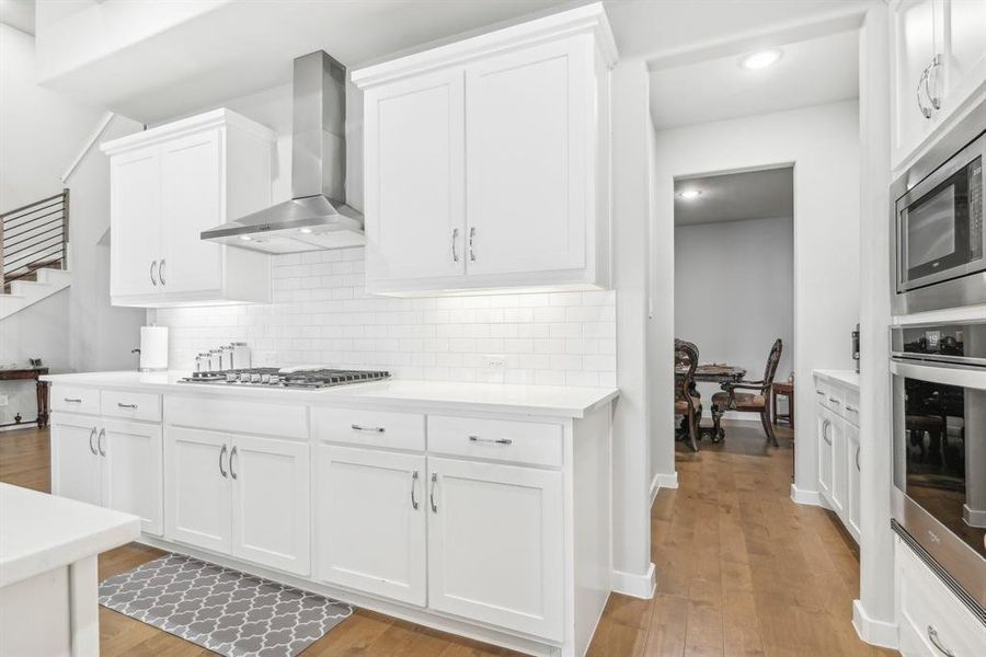 Kitchen with white cabinets, stainless steel appliances, light wood-type flooring, and wall chimney exhaust hood