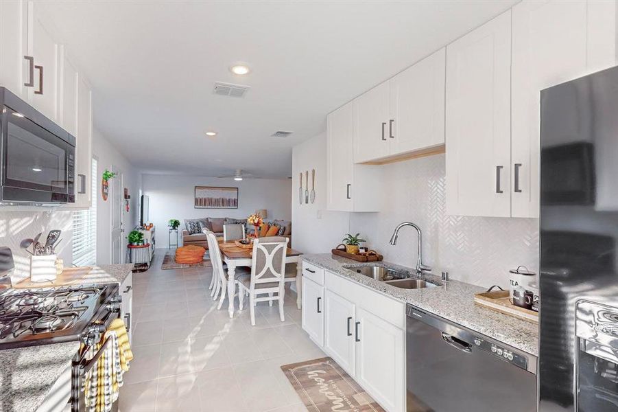 Kitchen featuring white cabinets, stainless steel appliances, sink, and light stone countertops