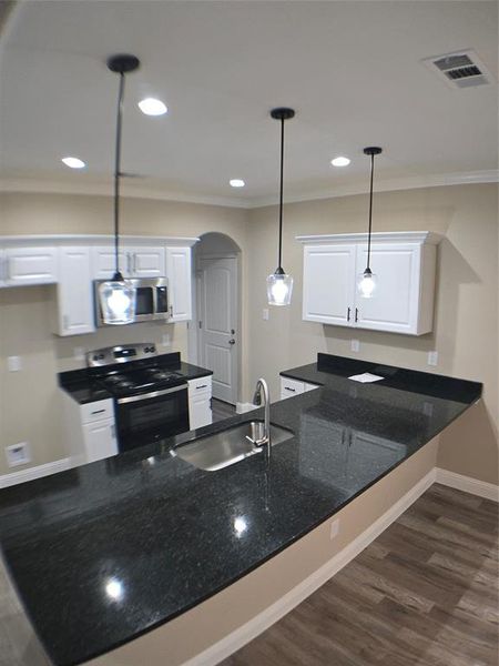 Kitchen with dark hardwood / wood-style floors, sink, white cabinetry, stove, and hanging light fixtures