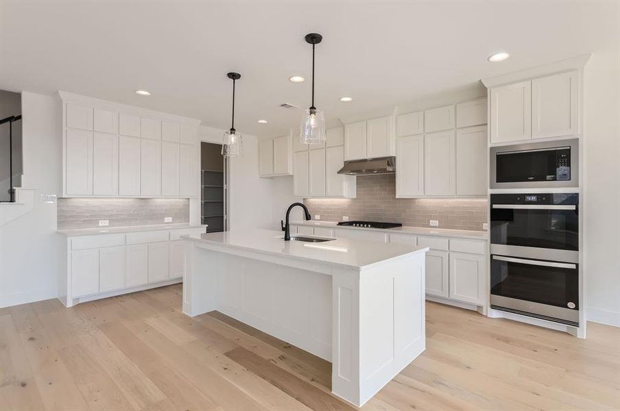 Kitchen featuring backsplash, sink, a kitchen island with sink, and white cabinets